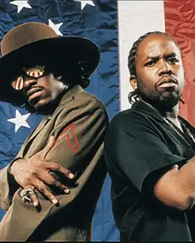 Outkast members André 3000 and Big Boi standing in front od American Flag