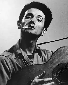 Folk singer Woody Guthrie with cigarette, holding guitar