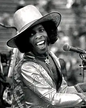 Sly Stone sitting at keyboard singing into microphone